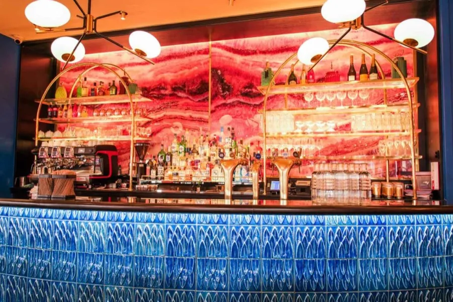The bar at Les Pipelettes du Boulevard, pink mural and blue-tiled counter