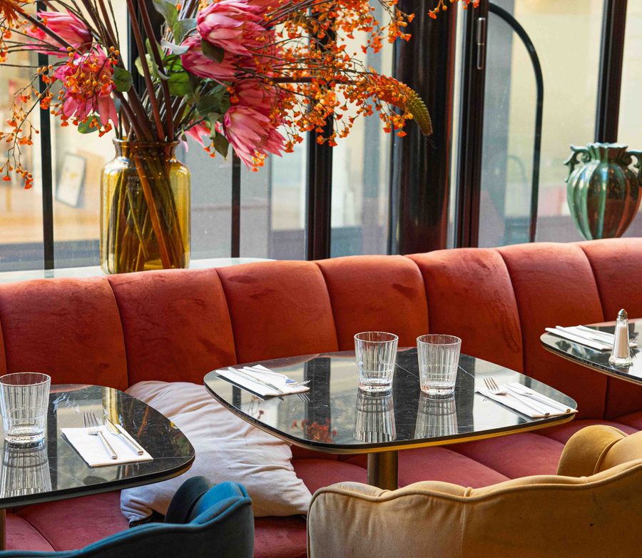 The dining room at Les Pipelettes du Boulevard, coral banquettes and seasonal flowers