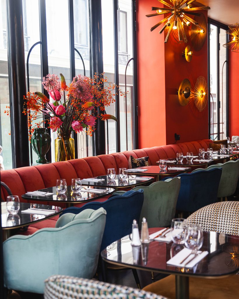 Coral banquette and seasonal flowers by the windows at Les Pipelettes du Boulevard
